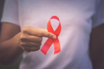Man holding red ribbon out in front of chest to signify HIV awareness